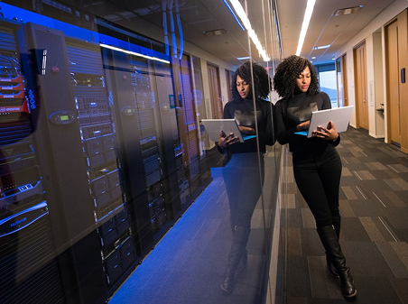 A woman working on her laptop while leaning against a dark glass window.